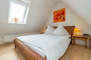 A bedroom with a large bed, a window with flowers, a painting, and a bedside lamp. - Meeresleuchten - Ab 2025 bei uns im Angebot, für Max. 4 Personen (Sylt)