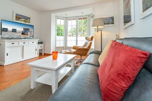 Un salon moderne avec un canapé, une table et une chaise. Il y a une fenêtre avec des stores, une lampe et un tableau au mur.