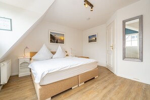 Une chambre à coucher avec un lit, deux tables de chevet, un grand miroir et deux tableaux encadrés accrochés au mur.