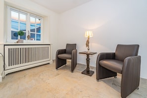 Ein Zimmer mit zwei Ledersesseln, einem kleinen Tisch mit Lampe, einem Heizkörper und einem Fenster mit Meerblick.