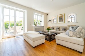 Amplia sala de estar con un gran ventanal corredera que da a un patio, una mesa de centro de madera oscura y un conjunto de sofá color beige.