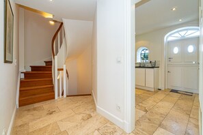 Ein modernes Interieur mit einer Holztreppe, einer Küche mit weißen Schränken und einem großen Bogenfenster.