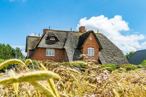 A traditional house with a thatched roof, brick walls, and a small window.
