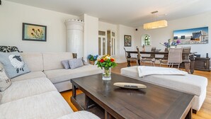 A modern living room with a sectional sofa, a coffee table with a vase of flowers, and a dining area with a table and chairs.