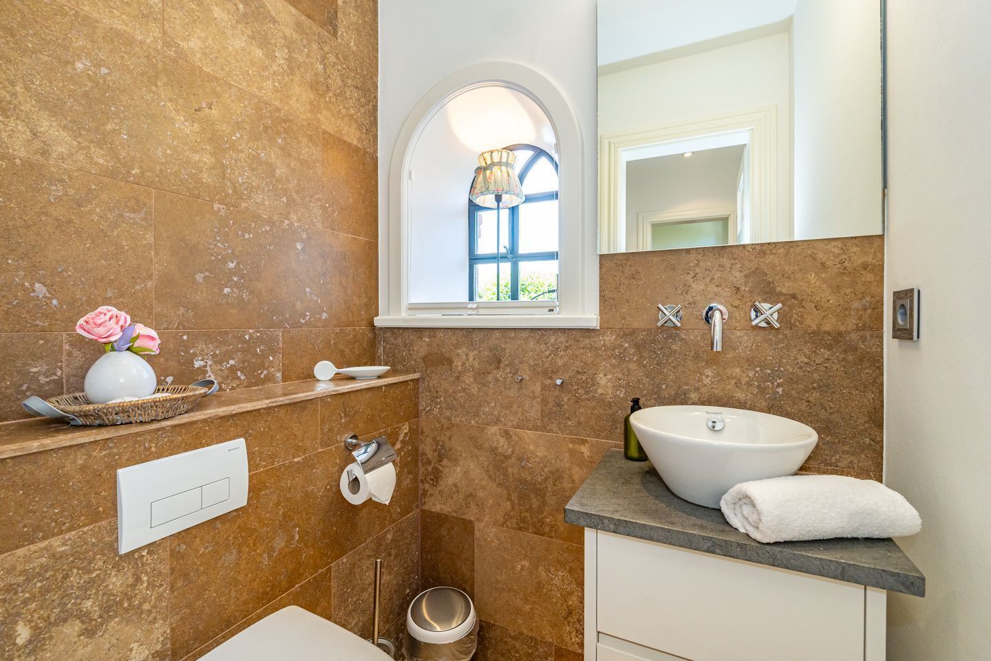 A bathroom with a large window, a white sink, and a mirror.