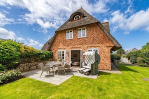 A brick house with a thatched roof, a patio with a table and chairs, and a well-maintained garden.
