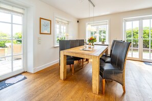 Een eetruimte met een houten tafel en zwarte lederen stoelen, grote ramen en uitzicht op groen buiten.