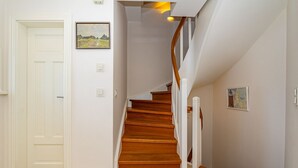 A staircase with wooden steps and white railings, leading to a landing with a door and a wall-mounted light switch. - Hüs bi Koog 1 - Vacation under thatch for up to 5 people. (Sylt)