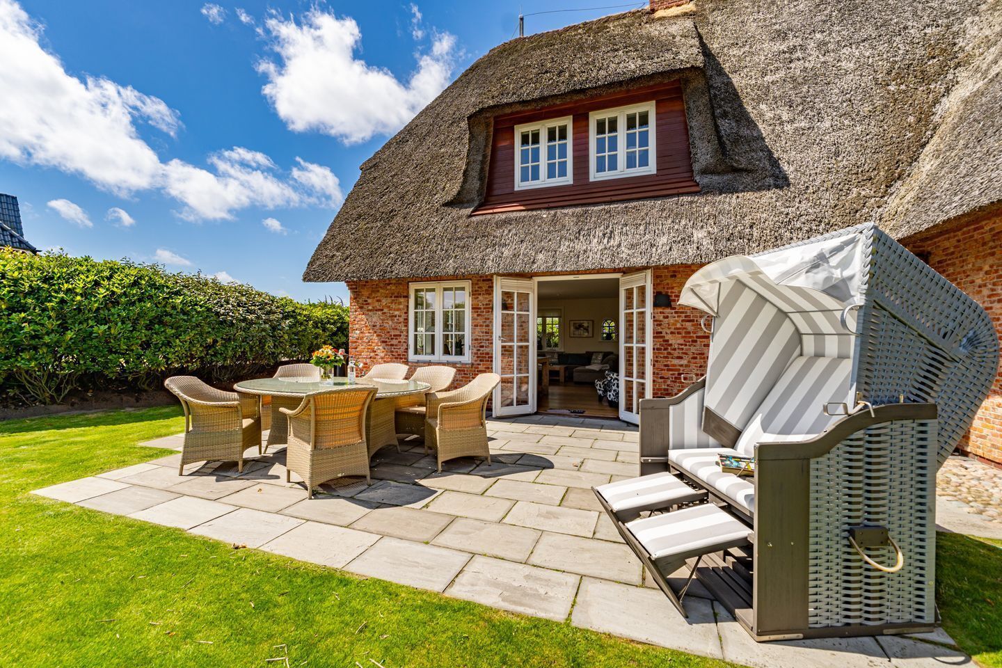 Ein Haus mit Strohdach, einer Terrasse, Korbmöbeln und einer überdachten Sitzgelegenheit im Freien.