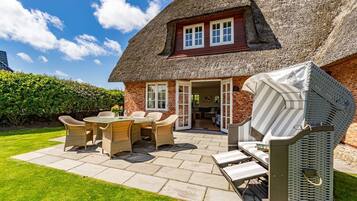 Ein Haus mit Strohdach, einer Terrasse, Korbmöbeln und einer überdachten Sitzgelegenheit im Freien.