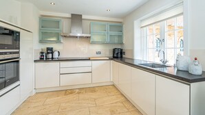 A modern kitchen with white cabinets, a stainless steel range hood, a built-in oven, a coffee maker, and a window with a view of a brick building. - Hüs bi Koog 1 - Vacation under thatch for up to 5 people. (Sylt)