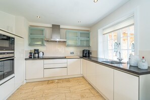 A modern kitchen with white cabinets, a stainless steel range hood, a built-in oven, a coffee maker, and a window with a view of a brick building. - Hüs bi Koog 1 - Vacation under thatch for up to 5 people. (Sylt)
