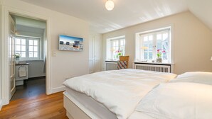 A bedroom with a large bed, a window with a view, and a door leading to a bathroom. - Hüs bi Koog 1 - Vacation under thatch for up to 5 people. (Sylt)