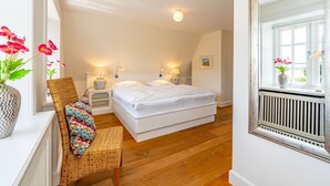 A bedroom with a bed, bedside tables, a chair, a window, and a radiator. - Hüs bi Koog 1 - Vacation under thatch for up to 5 people. (Sylt)