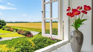 Ein Fenster mit Blick auf eine grüne Landschaft und eine Vase mit roten Blumen auf einer weißen Oberfläche.