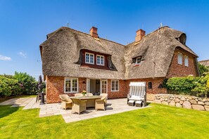 A large house with a thatched roof, a brick exterior, and a well-maintained lawn.