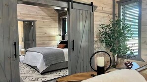 Ein Holzinterieur mit einem Bett, einer Schiebetür, einer Pflanze und einer Kerze auf einem Tisch.