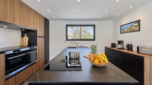 A modern kitchen with a central island, black countertops, wooden cabinets, a built-in oven, and a window providing a view of the outdoors. - Denneweiller by Interhome (Denneville)