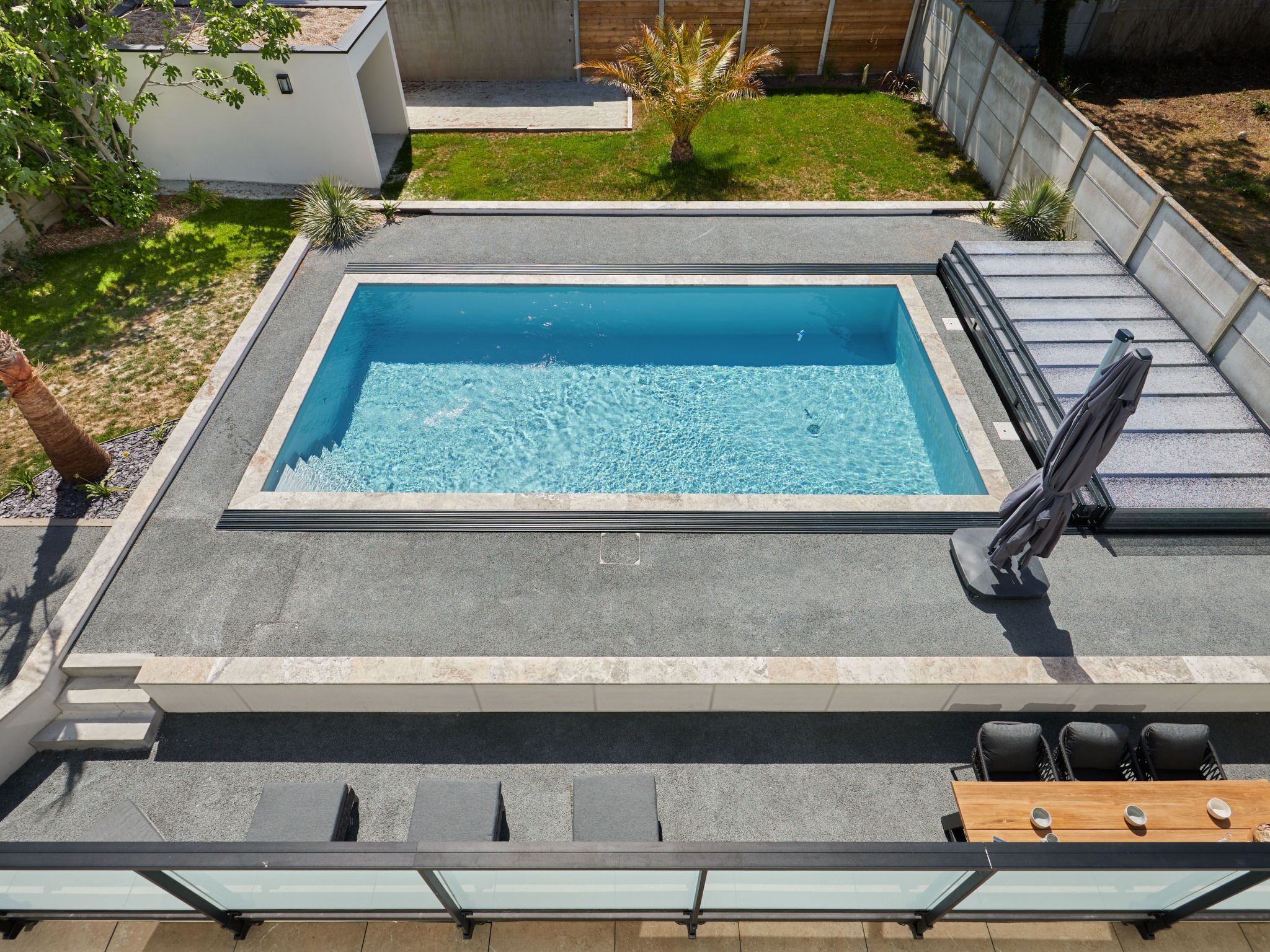 Une piscine rectangulaire à l’eau d’un bleu limpide, entourée d’une terrasse en béton.
