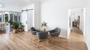 A modern dining area with a glass table, four grey chairs, and wooden flooring.