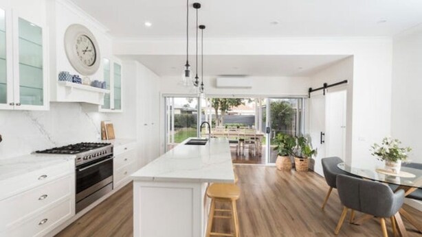 A modern kitchen with white cabinetry, a central island, and a dining area with a table and chairs.