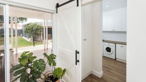 A modern kitchen with white cabinets, a washing machine, and a wooden floor.