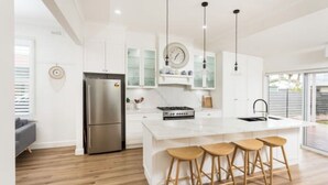 A modern kitchen with white cabinetry, a stainless steel refrigerator, a central island with stools, and pendant lighting.