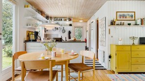 Een lichte keuken met houten kastjes, een geel kastje, en een eethoek met een tafel en stoelen.