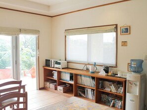 Une pièce comprenant un bureau en bois, des étagères, un four à micro-ondes, une bouilloire et un distributeur d’eau.