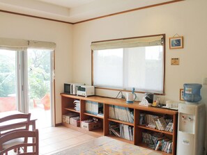 Une pièce comprenant un bureau en bois, des étagères, un four à micro-ondes, une bouilloire et un distributeur d’eau.