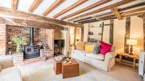 A cozy living room with exposed wooden beams, a brick fireplace, a sofa with cushions, a coffee table, and a bookshelf. - Anchor Cottage, Orford (Orford)