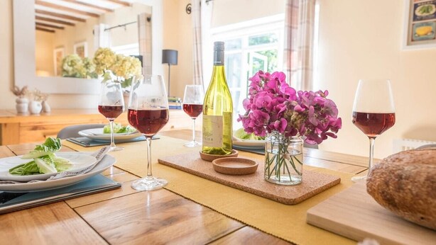 A dining table with wine glasses, a bottle of wine, and a vase of flowers. - Anchor Cottage, Orford (Orford)