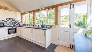 A modern kitchen with white cabinets, a black countertop, and a large window. - Anchor Cottage, Orford (Orford)