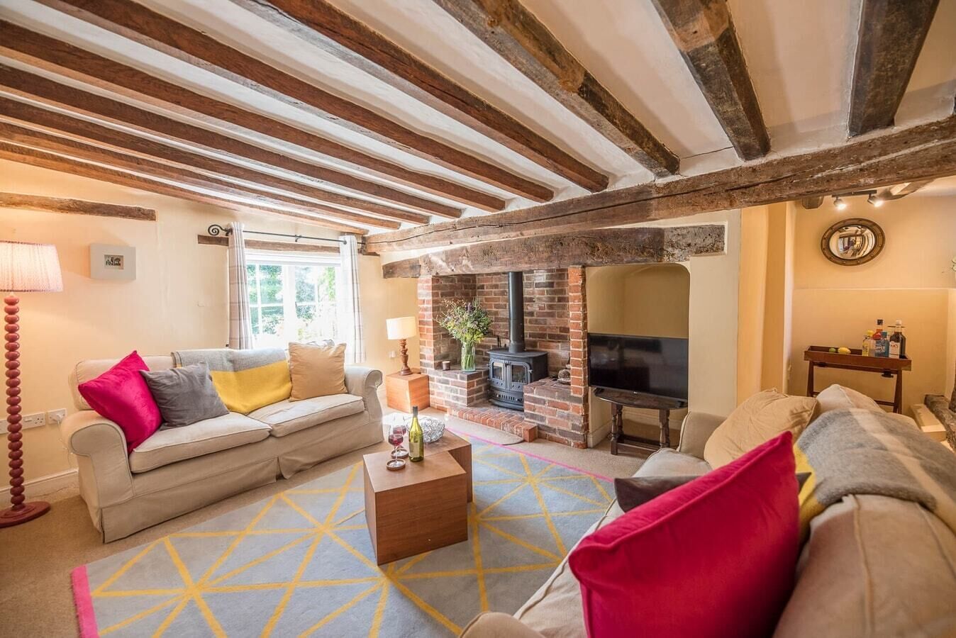 A cozy living room with exposed wooden beams, a brick fireplace, and a television.