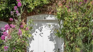 A white wooden gate with a number "21" on it, surrounded by lush greenery and purple flowers. - Anchor Cottage, Orford (Orford)