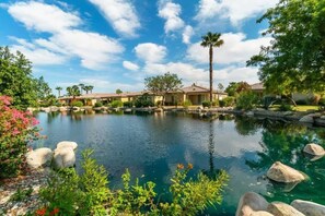 A residential area with a clear blue sky, a small pond, and houses with red-tiled roofs. - Lake View 3BR | Resort Pools at Indian Palms (Indio)