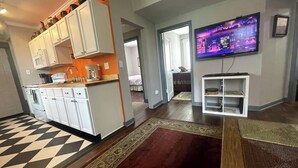 Moderni keittiö, jossa on valkoiset kaapit, mikroaaltouuni ja kahvinkeitin. Ruokailutilassa on punainen matto ja seinälle asennettu televisio.