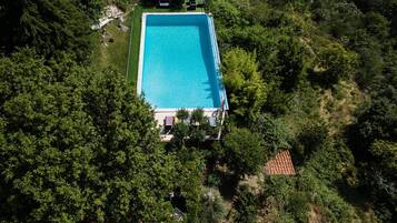 Vista aerea di una piscina rettangolare immersa nel verde, con un piccolo edificio e alcuni sedili da esterno.