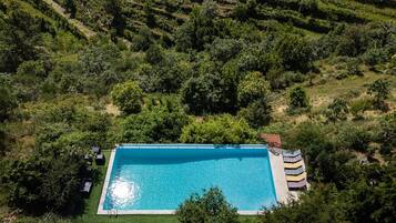 Vista aérea de una piscina rectangular rodeada de exuberante vegetación y campos en terrazas.
