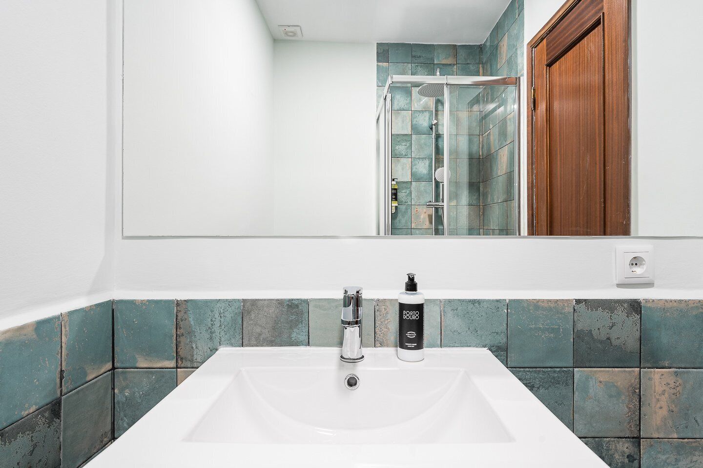 Un baño con un lavabo blanco, un espejo y una zona de ducha con puertas de cristal.
