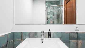 Un baño con un lavabo blanco, un espejo y una zona de ducha con puertas de cristal.
