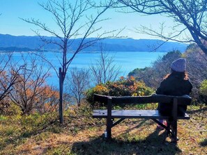 A person sitting on a bench overlooking a body of water with mountains in the distance. - Waka no Yado  Kanade   Private accommodation   - Waka no Yado Kanade / Wakayama Wakayama (Wakayama)