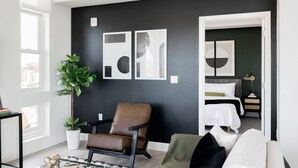 A modern living room with a black accent wall, a brown leather chair, a white sofa, and a large green plant. - Serenity in Style | Espadin LoHi (Denver)