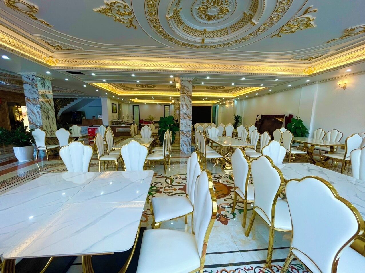 A banquet hall with marble flooring, white and gold chairs, and a central column.