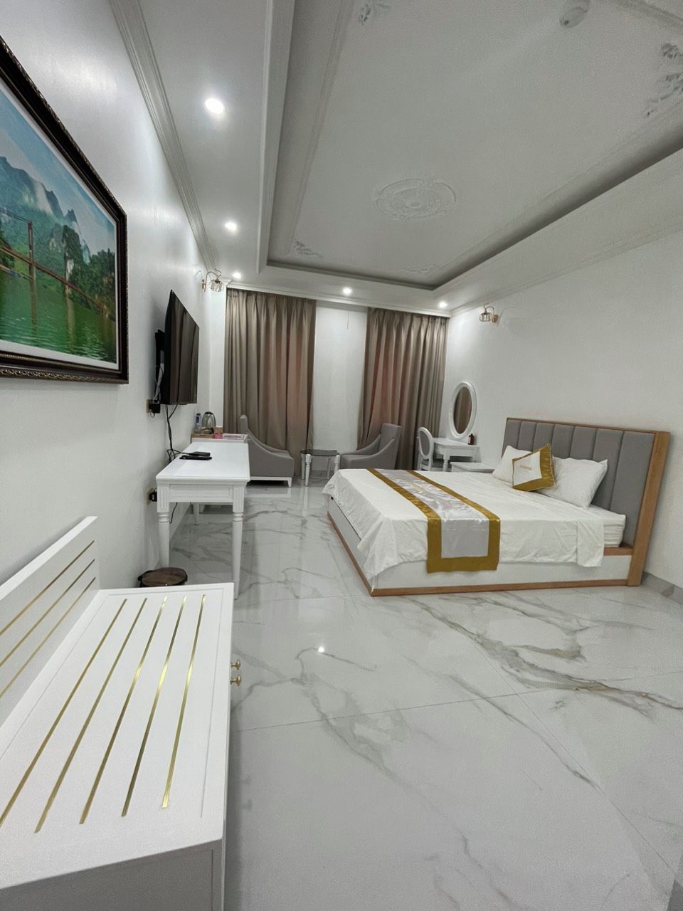 A modern hotel room with a bed, bedside table, chair, desk, and a television.