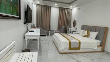 A modern hotel room with a bed, bedside table, chair, desk, and a television.