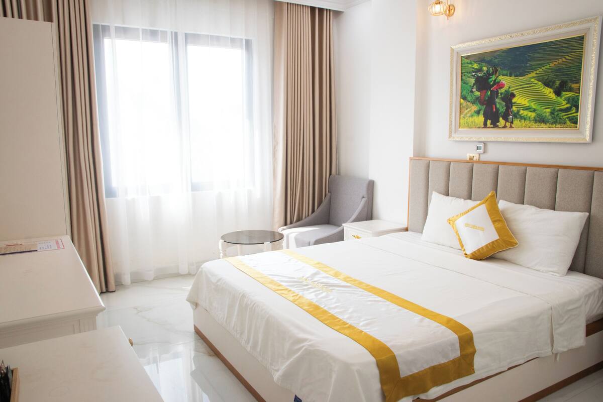 Habitación de hotel con una cama grande, una silla, una mesita y un cuadro en la pared.