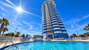 Un hôtel doté d’une grande piscine, d’un soleil radieux et d’un ciel d’un bleu limpide.