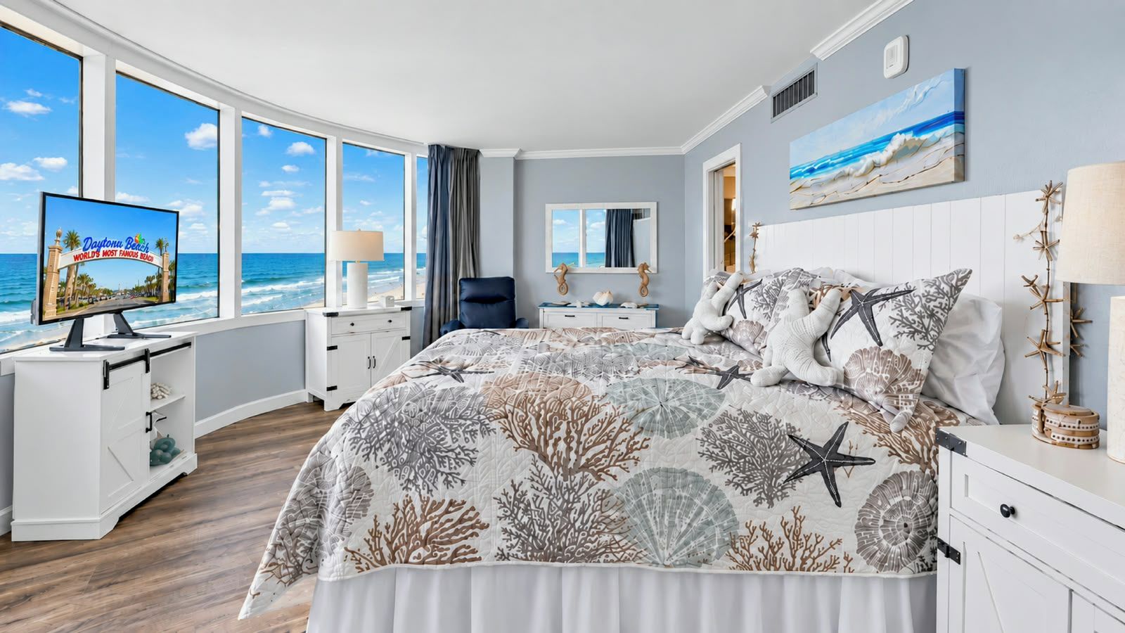 A bedroom with a large bed, a TV, and a view of the ocean.