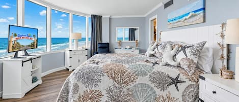 A bedroom with a large bed, a TV, and a view of the ocean.
